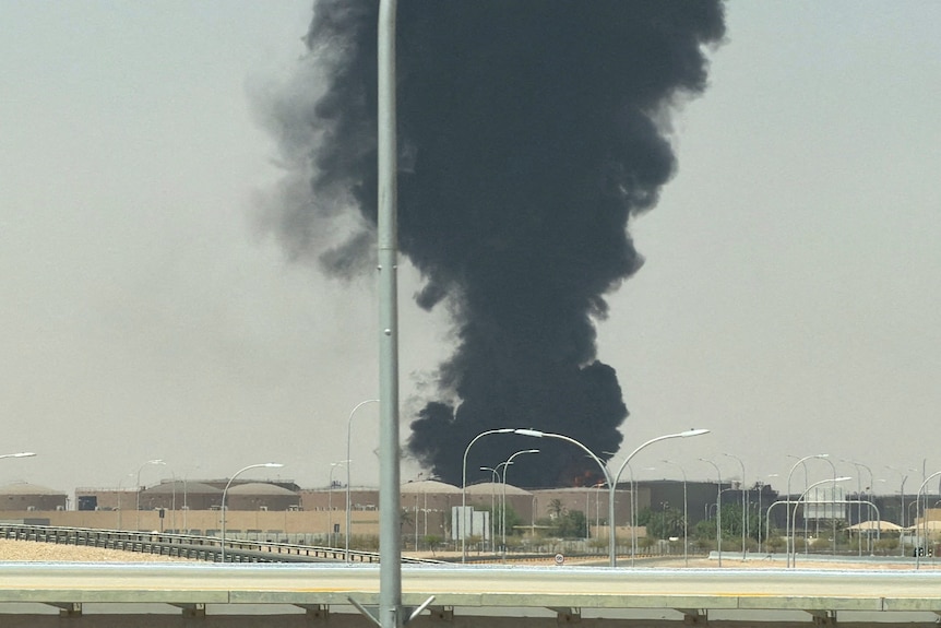 A large plume of black smoke rising from an area with fuel tanks