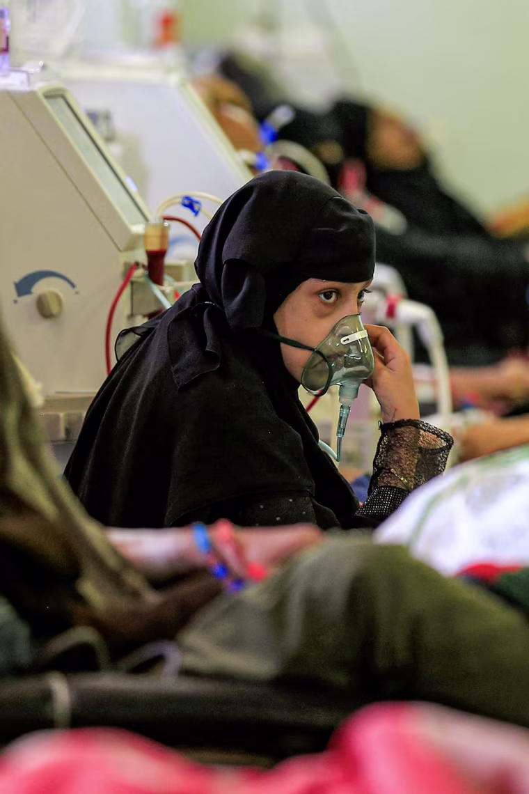 A young girl holds a respirator mask over her face inside a crowded hospital room.