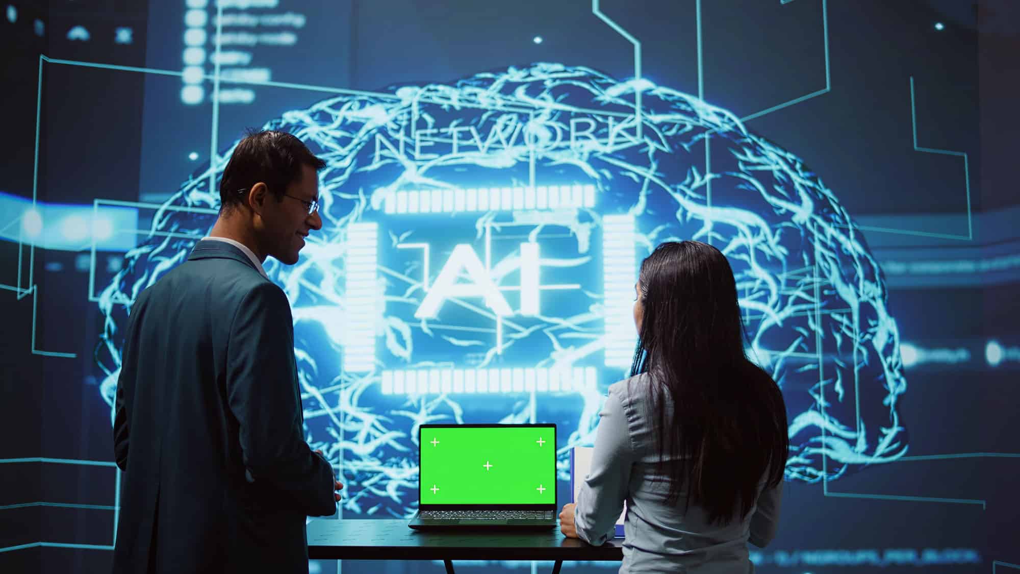 Homem e mulher na frente de um notebook com uma projeção de IA ao fundo.