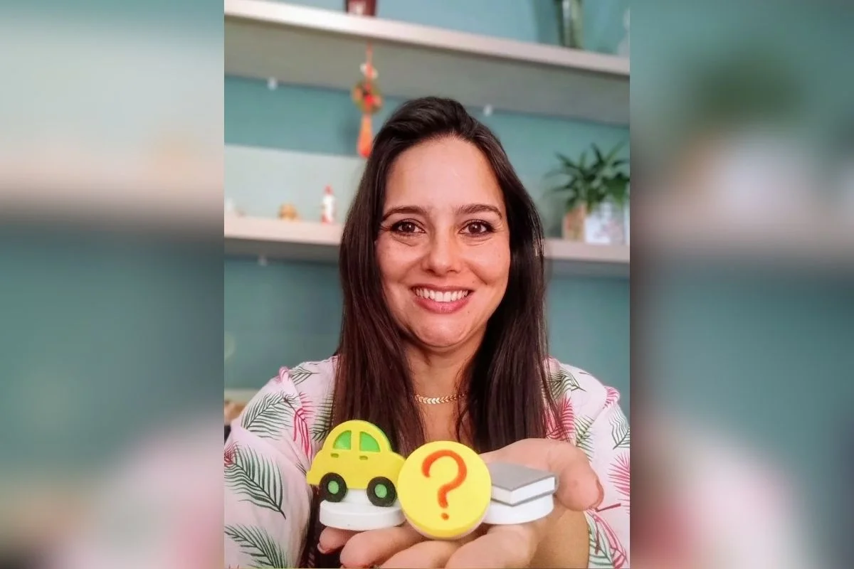 Foto colorida de mulher segurando objetos nas mãos e sorrindo.