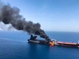 An oil tanker at sea is on fire with a large cloud of smoke coming out of it