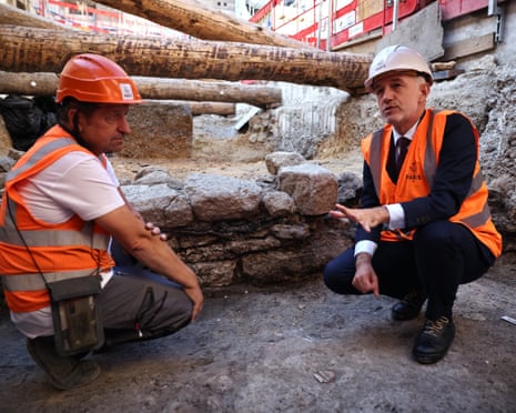 Paris Mayor Emmanuel Gregoire crouches with an archaeologist beside an excavated ancient stone wall