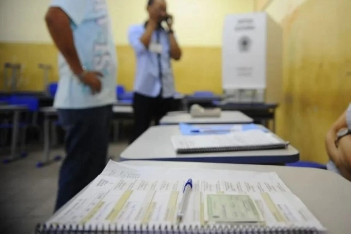 Imagens coloridas mostram mesa de votação e mesários em pé, com cabine de votação ao fundo