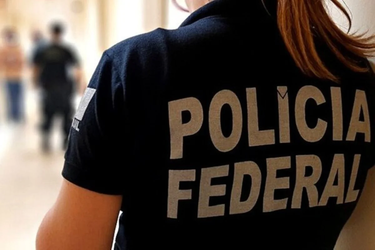 Imagem colorida mostra mulher de costas vestindo colete preto onde está escrito Polícia Federal - Metrópoles