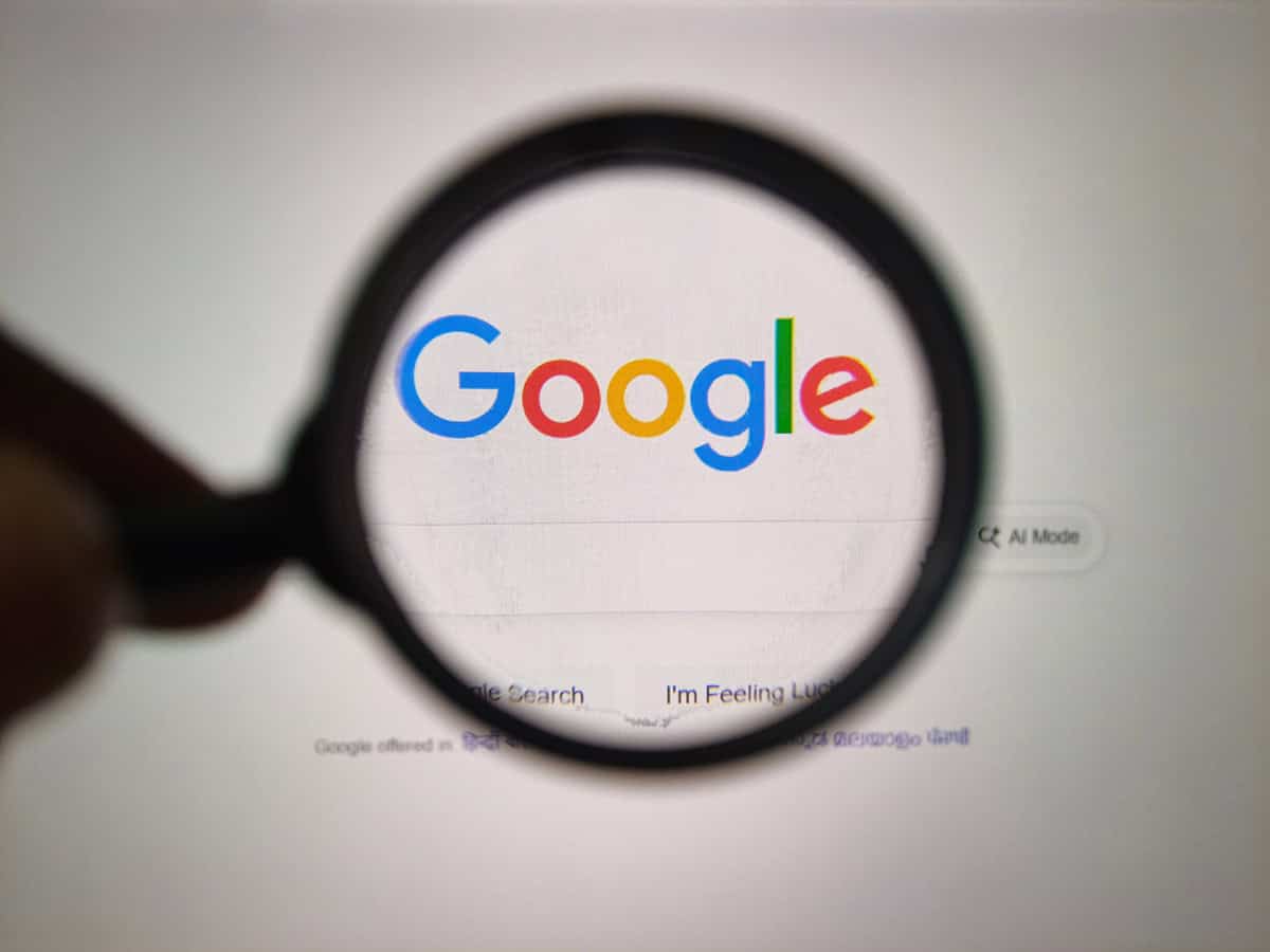 Um close-up de uma lente de aumento segurada sobre o logotipo icônico do Google exibido em um monitor de computador, destacando o poder da pesquisa.