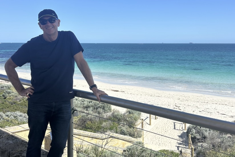 A man wears sunglasses and a hat as he stands by the beach