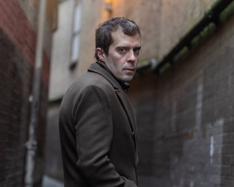 Roman Dobrokhotov in a brown coat, looking over his shoulder in a narrow alley