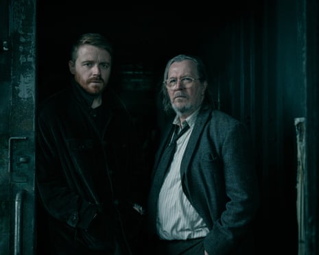 Jack Lowden and Gary Oldman stand together in a dim, shadowy doorway in Slow Horses.