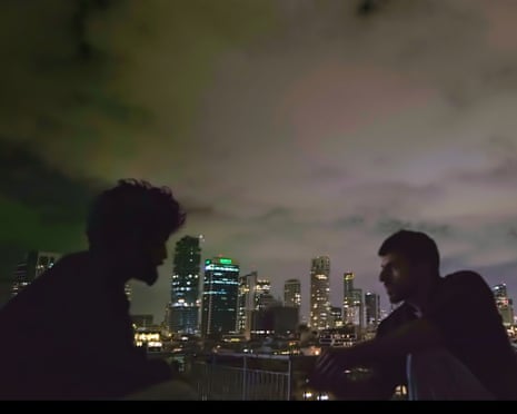 Two people in silhouette sits looking out over a city skyline lit up at night